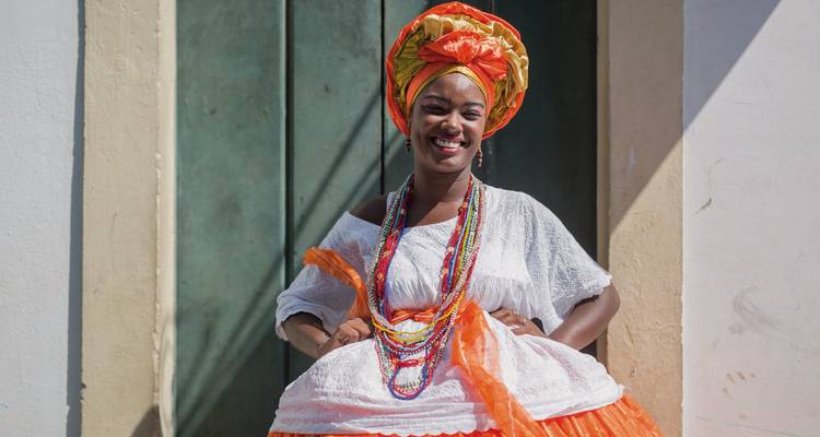 Una mujer sonriente con vestimenta tradicional parada contra una pared colorida.