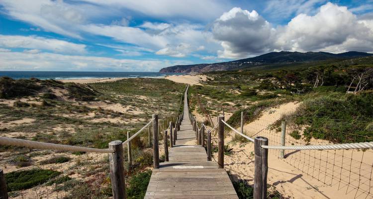 Passerelle en bois menant à une plage de sable sous un ciel bleu.