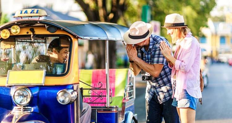 Pareja interactuando con conductor de tuk-tuk en una ciudad.