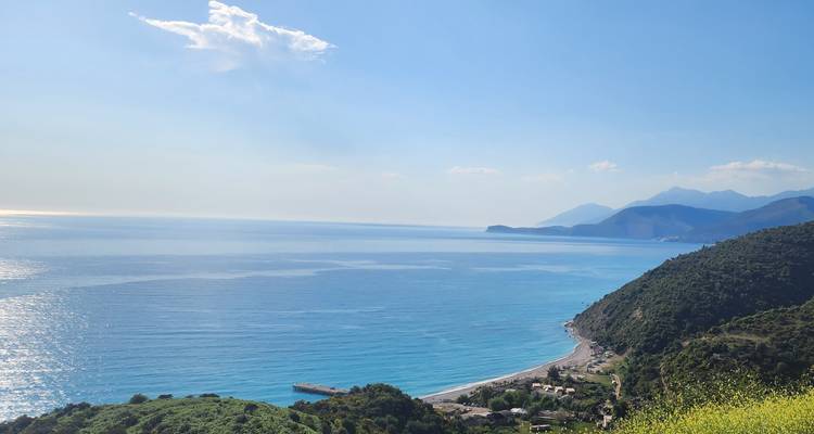 Panorama côtier expansif d'eaux bleues calmes, de promontoires et de montagnes lointaines et brumeuses sous un ciel dégagé.