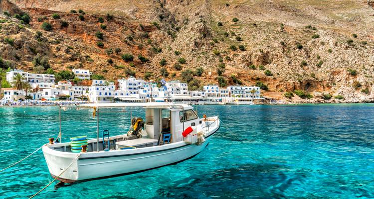 Small fishing boat on clear blue waters near a coastal town.