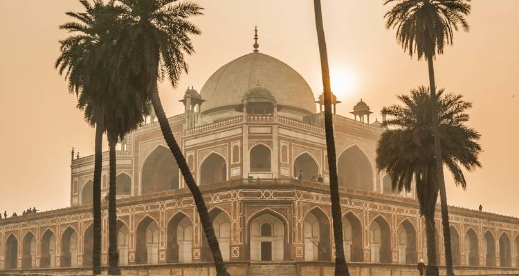 Humayun’s Tomb silhouetted in hazy sunrise light framed by tall palm trees.