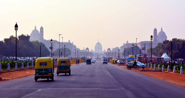 Wide boulevard of New Delhi’s government district with auto-rickshaws driving toward Rashtrapati Bhavan in light haze.
