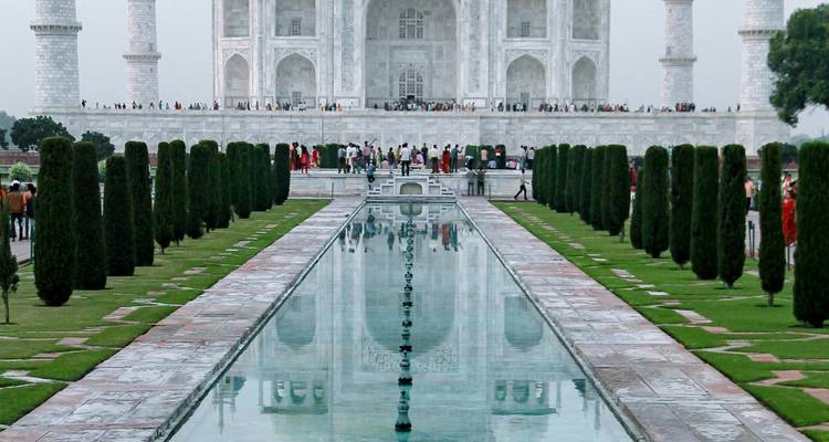 Iconic reflecting pool leading to the Taj Mahal crowded with visitors along manicured cypress trees.