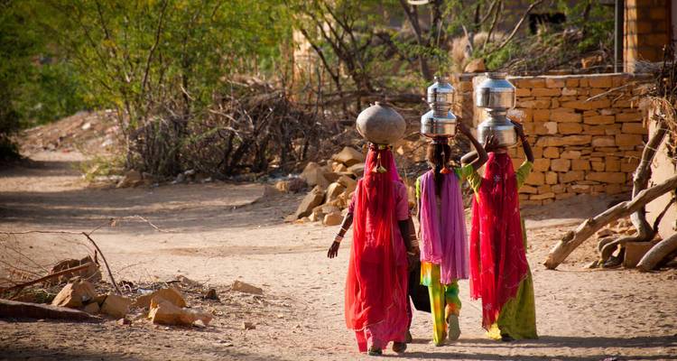 Des femmes portant des pots sur la tête marchant dans un village.