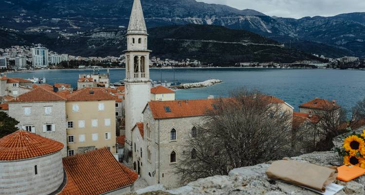 Vue panoramique sur la vieille ville aux toits de terre cuite de Budva avec son clocher et sa baie encadrée par des montagnes escarpées.