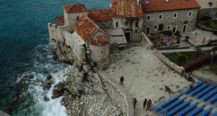 Citadelle au sommet des falaises et église en pierre perchées au-dessus des vagues déferlantes à Budva, vues d'en haut.