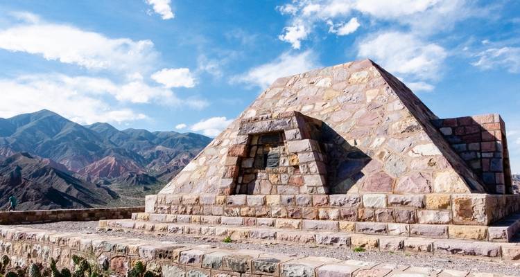 Structure pyramidale en pierre avec des montagnes colorées en arrière-plan.