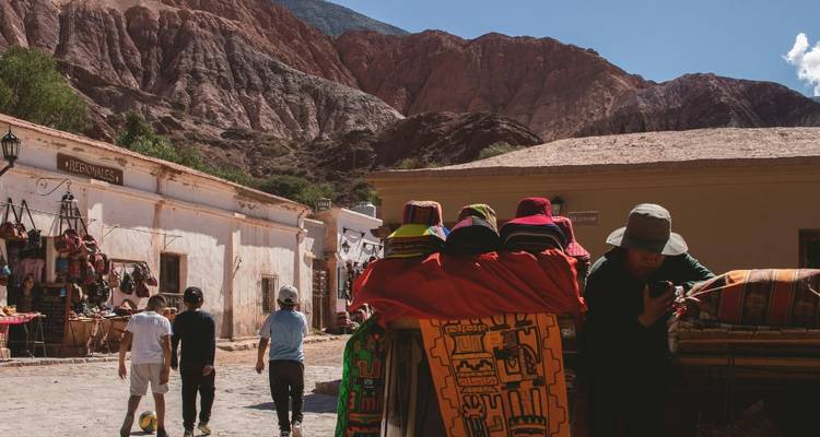 Marché de village de montagne avec des textiles colorés et des collines en arrière-plan.