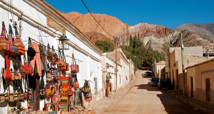 Route de village rustique avec des sacs colorés suspendus devant une boutique dans une région montagneuse.