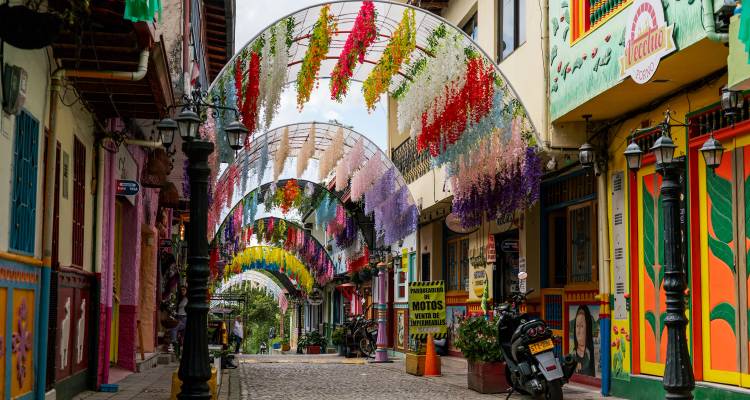Color-splashed pedestrian street lined with vibrant facades and archways draped in hanging flower garlands.