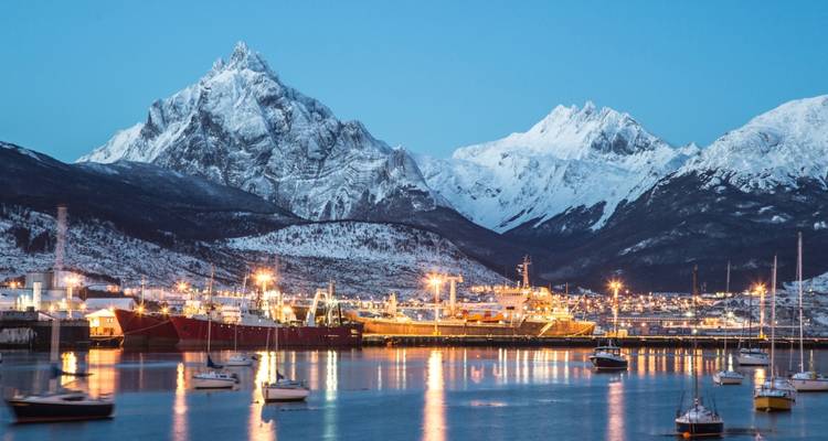Port avec éclairage et montagnes enneigées au crépuscule.