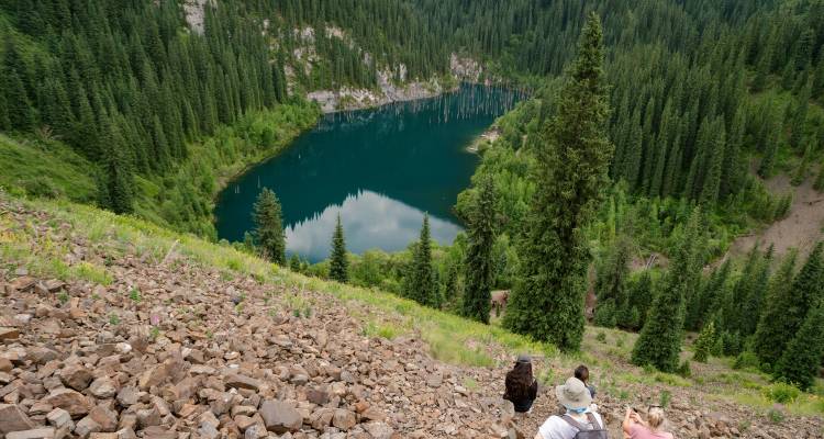 Les randonneurs descendent vers un lac alpin turquoise entouré d'une forêt de conifères dense au Kazakhstan.