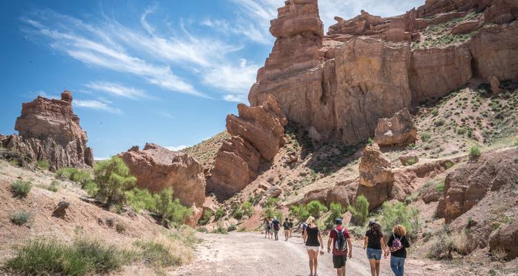 Een wandelgroep volgt een stofig pad onder de imposante zandstenen wanden van de Charyn Canyon.