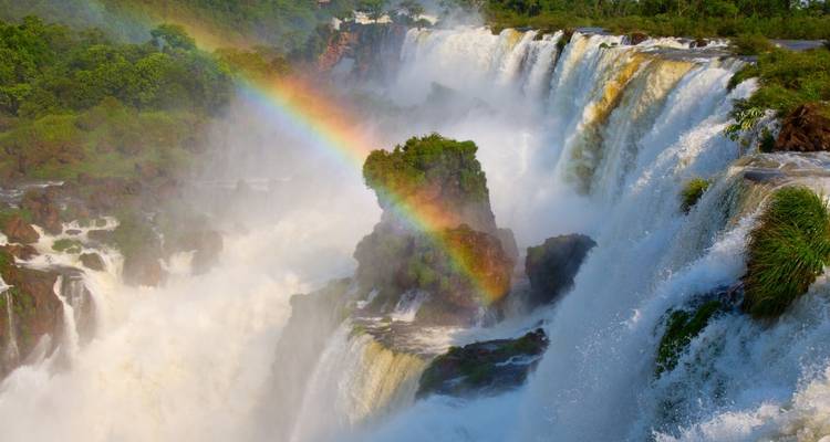 Rainbow forming over powerful waterfalls with spray.