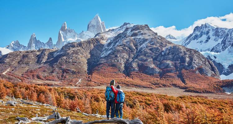 Dos excursionistas mirando una cordillera con árboles de otoño.
