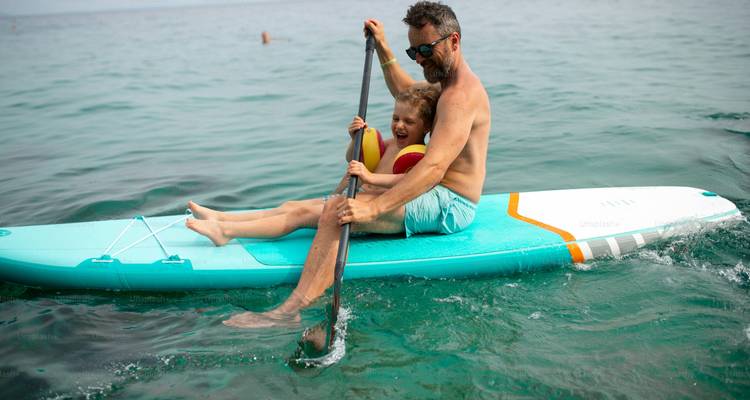 A father and child on a paddleboard in the sea.