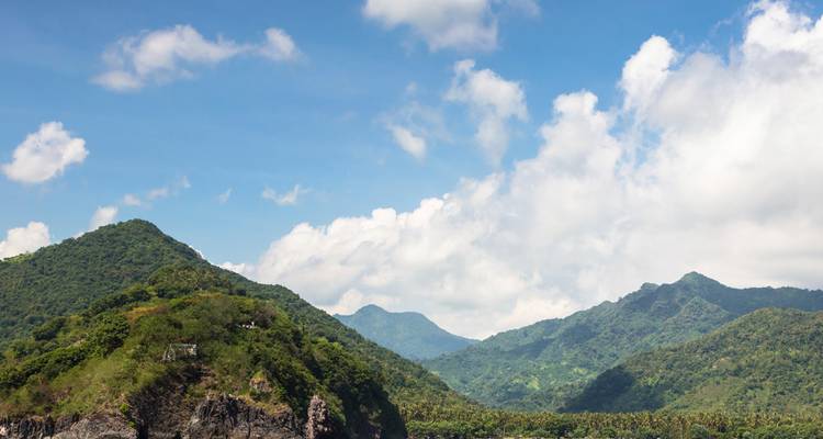 Colinas verdes cubiertas de selva bajo un cielo azul brillante con nubes blancas esponjosas.