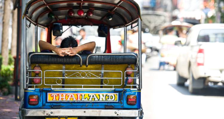 Achterkant van een tuk-tuk met een chauffeur die rust, gericht op de straat vooruit.
