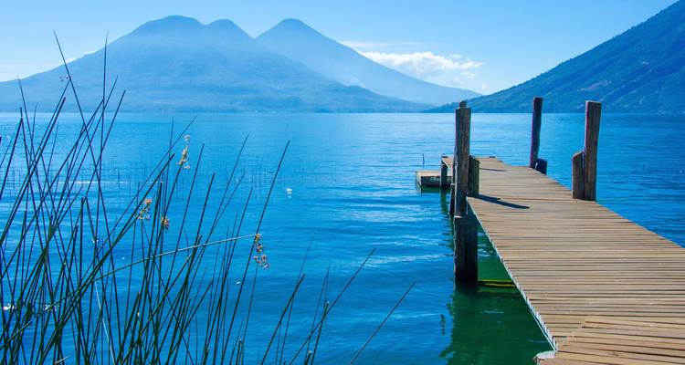 Otra vista de un muelle de madera que se extiende sobre las aguas cristalinas del Lago Atitlán con volcanes a lo lejos.