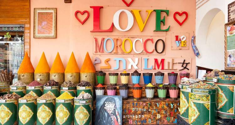 Especias exhibidas en recipientes coloridos con una pared decorativa detrás.