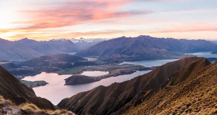 Panoramisch zonsopgang boven alpiene meren en ruige bergtoppen, gezien vanaf een hoge bergrug boven Wanaka.