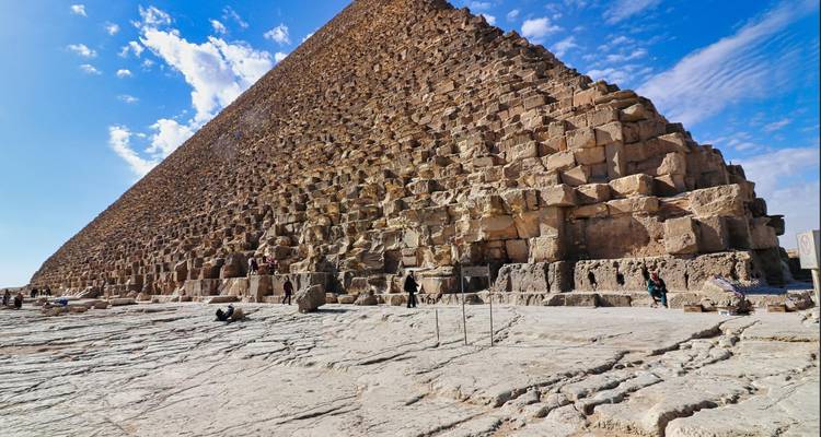 Massieve kalkstenen blokken vormen de Grote Piramide onder een heldere blauwe hemel.