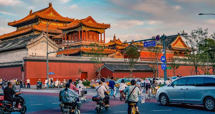 Calle bulliciosa fuera de los muros de la Ciudad Prohibida con ciclistas, peatones y autos al atardecer en Beijing.
