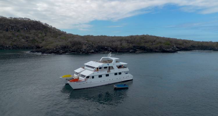 A white motor yacht anchored in a calm bay surrounded by low, green islands under a partly cloudy blue sky.