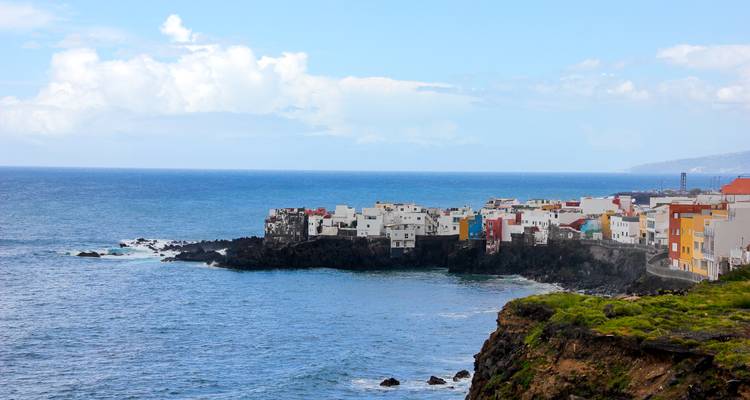 Un pueblito costero lleno de color con fachadas blancas se asoma desde las rocas volcánicas oscuras frente al Atlántico.