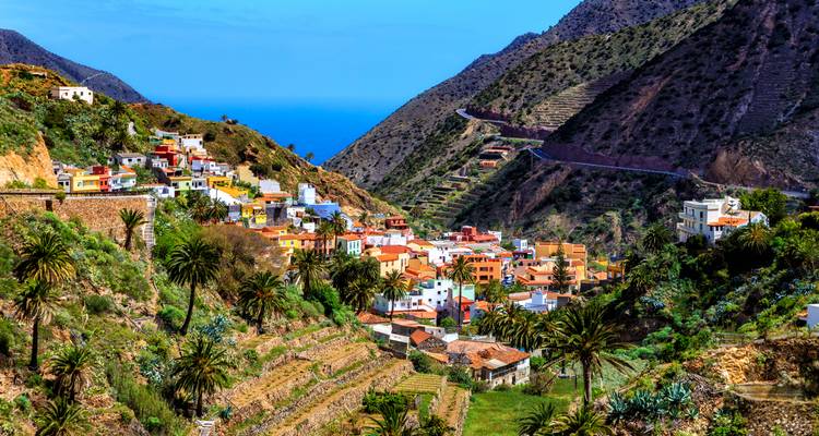 A picturesque valley village of colorful houses, terraced fields and palms rises toward the azure sea.