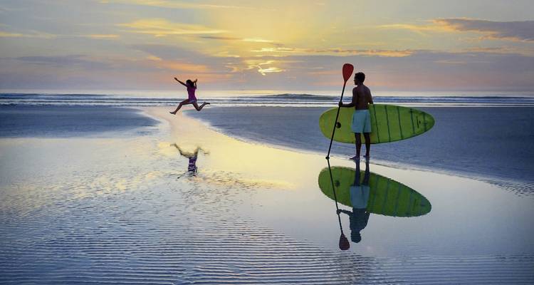 Surfer und Kind spielen am Strand bei Sonnenuntergang.