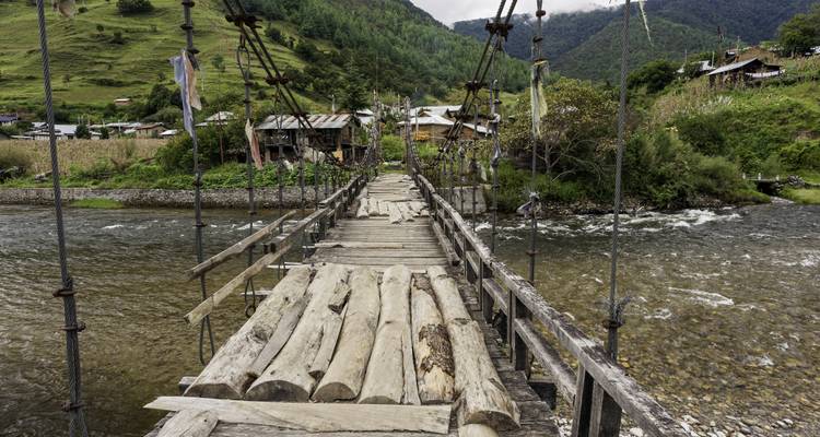 Rope suspension bridge over a river with small village in the background.