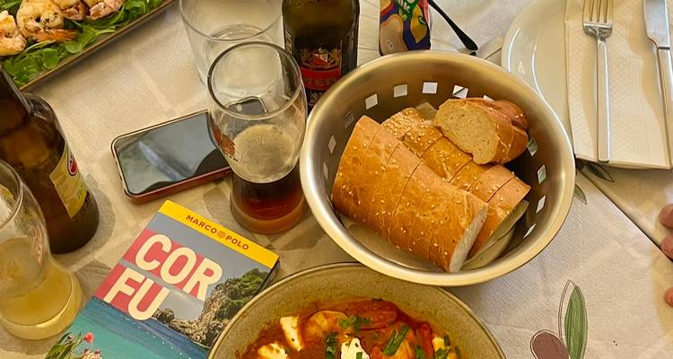 Tisch mit Essen und Getränken gedeckt, Korfu-Reiseführer sichtbar.