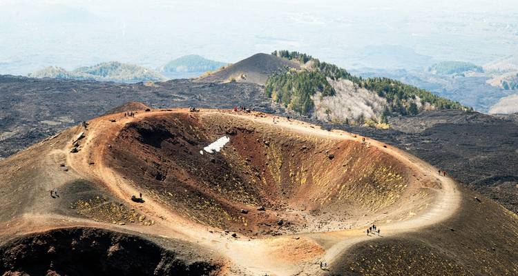 Un cráter volcánico con senderos visibles y pequeñas figuras caminando.