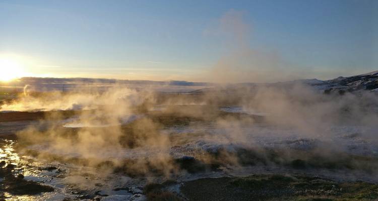Steamy geothermal field with sunset in the background.