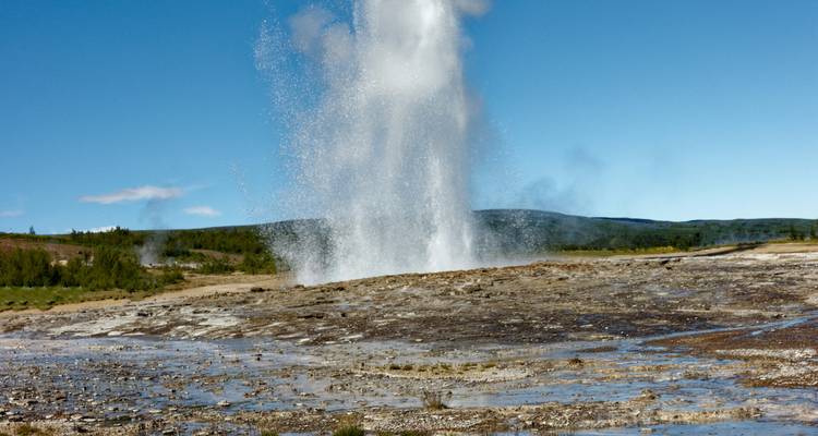 Geyser erupting with water spray against clear blue sky.