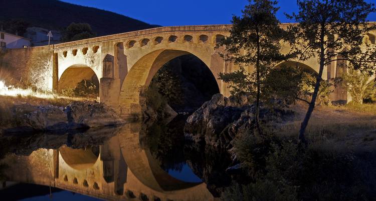 Puente histórico de piedra con iluminación nocturna reflejándose en el agua