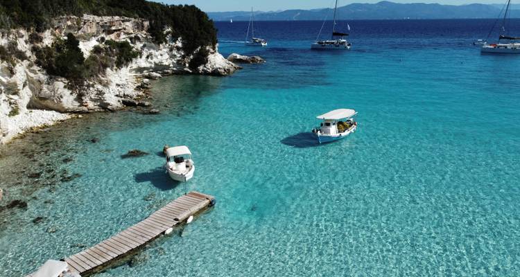 Barcos en agua azul cristalina cerca de la costa rocosa.