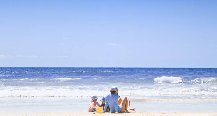 Dos personas sentadas en una playa mirando hacia el mar.