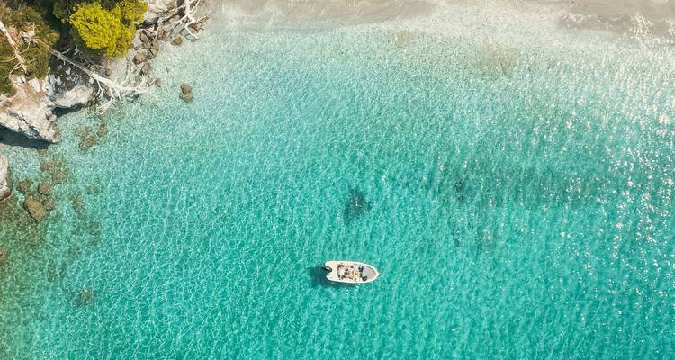 Vista aérea de un pequeño bote en agua turquesa cristalina.