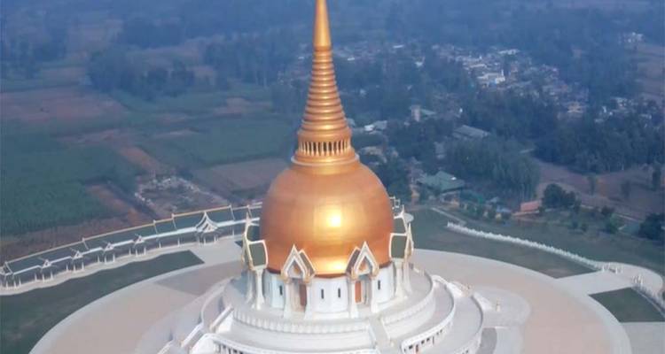 A large golden stupa in a complex of buildings, surrounded by rural landscape.