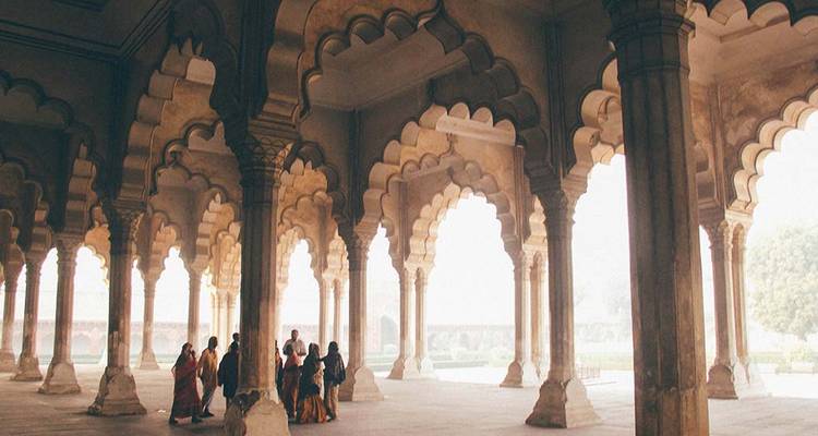 People walking under arches of a historical building.