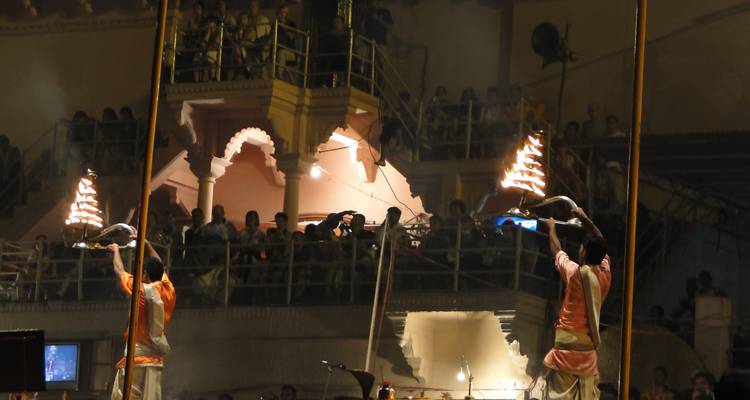 People performing evening rituals near a river with lit fire offerings.