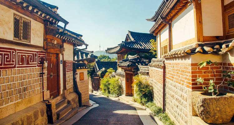 Village traditionnel coréen hanok avec vue sur les toits de tuiles et une tour au loin.