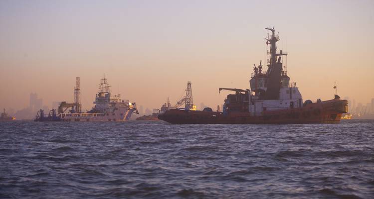 Barcos y embarcaciones en el agua con el telón de fondo del horizonte de una ciudad al atardecer.