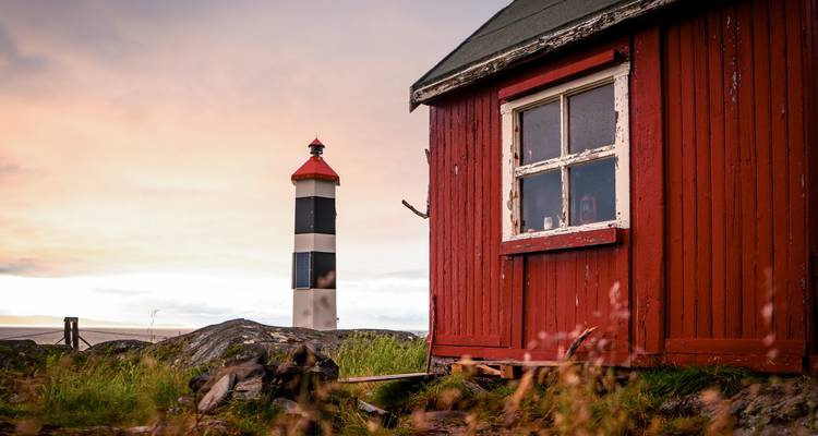 Gros plan d'un bâtiment rouge et d'un phare au coucher du soleil.