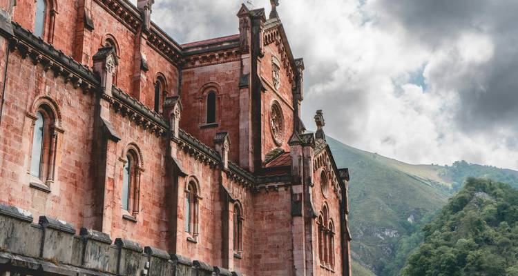 Vue de côté d'une cathédrale historique par une journée nuageuse avec des montagnes.