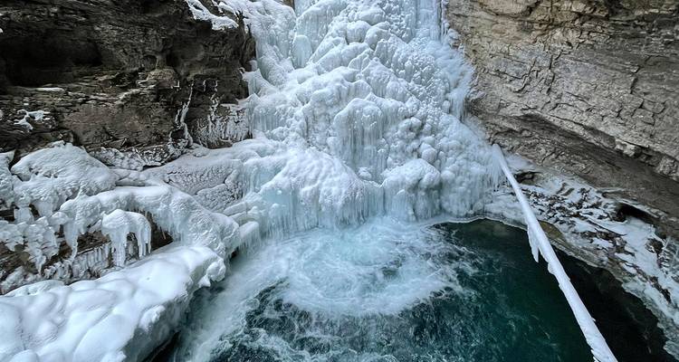 A frozen waterfall cascades into an icy turquoise pool within Johnston Canyon.