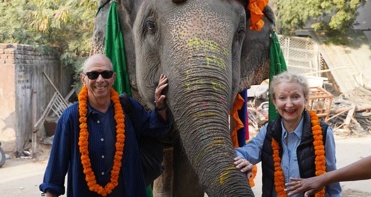 Two people with an elephant, wearing garlands.